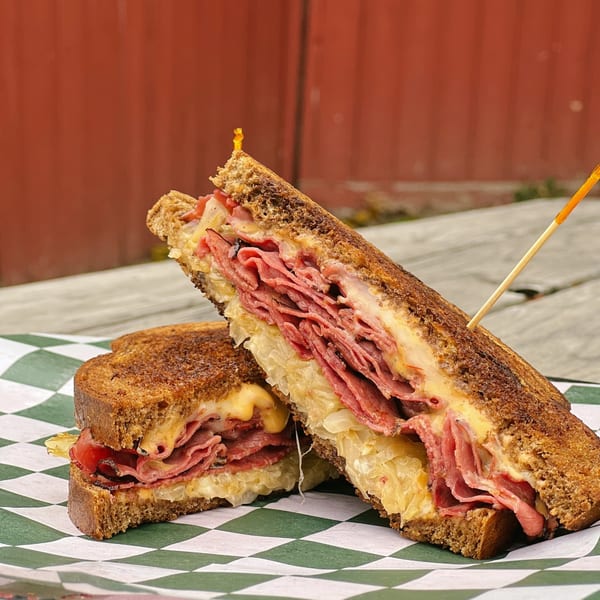 A Country Corners Deli Reuben sandwich, cut in half, with corned beef, sauerkraut, and melted cheese.