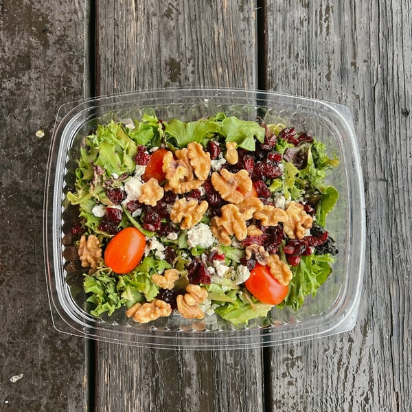 A Country Corners Deli salad with greens, walnuts, cranberries, feta, and cherry tomatoes in a plastic container.