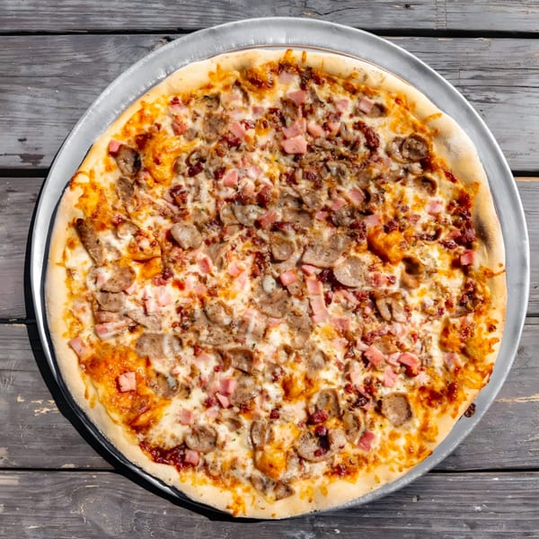 A Country Corners Deli pizza with sausage, ham, and bacon on a metal tray.