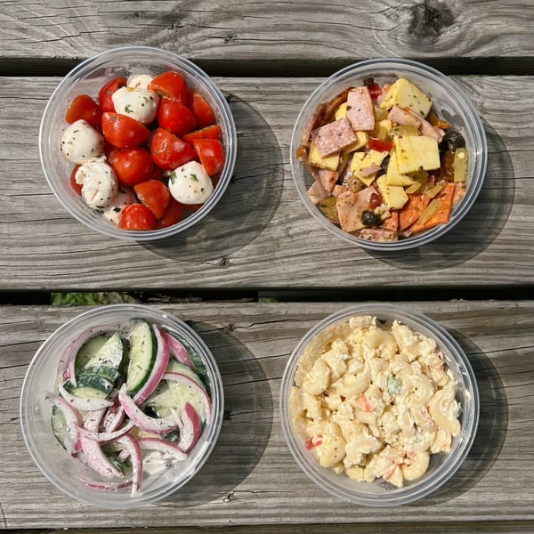 Four deli salads in clear containers: caprese, antipasto, cucumber onion, and macaroni salad on a wooden table.