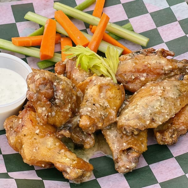 Country Corners Deli's garlic parmesan wings with celery, carrots, and ranch dressing on checkered paper.