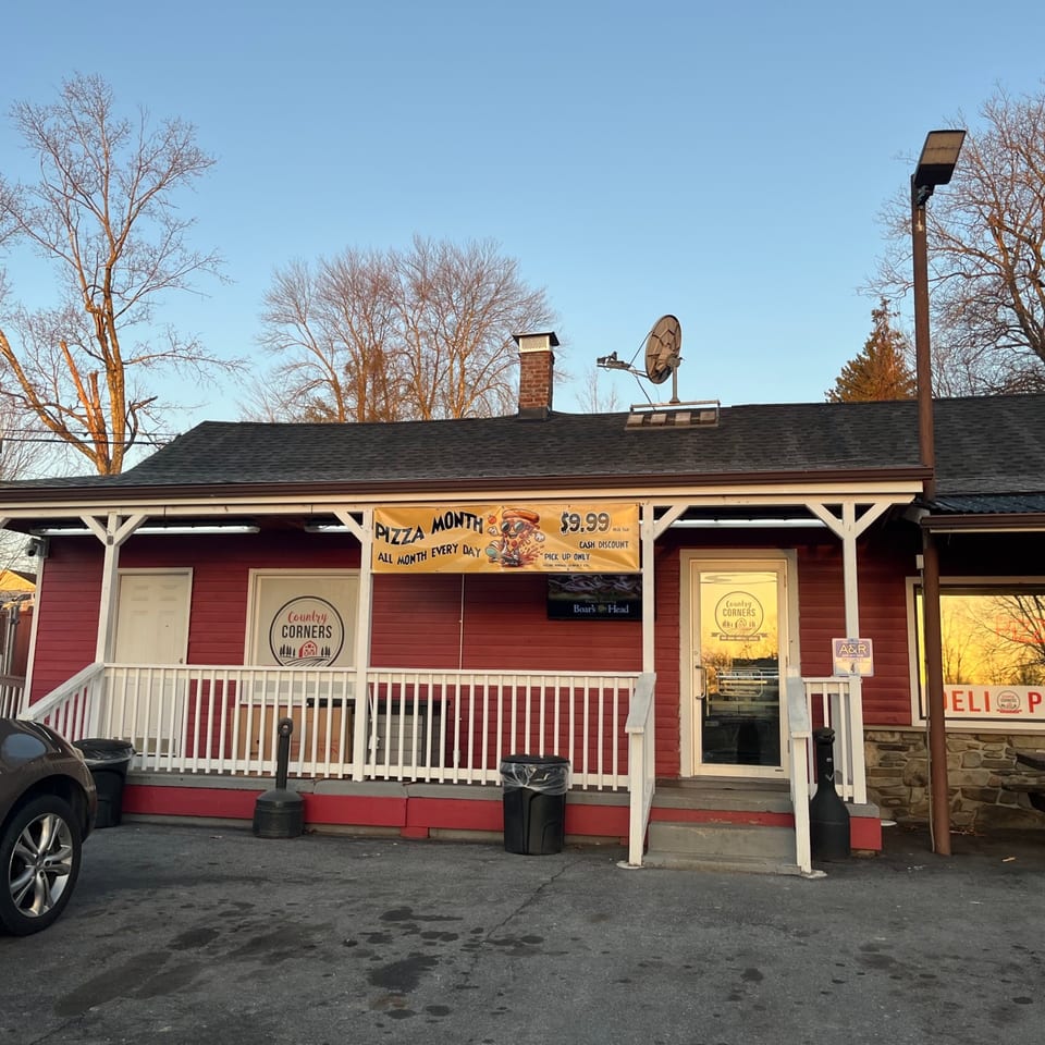 Exterior of Country Corners Deli, a red building with a white porch and a "Pizza Month" banner.